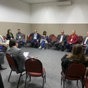 14 pessoas reunidas em círculo em uma sala de reuniões