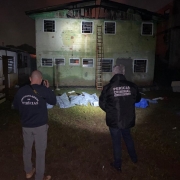 Dois homens com jaqueta da perícia criminal em frente a prédio, de noite