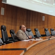 Homem sentado, falando no microfone para a plateia 