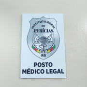 Placa identificando a sala do Posto Médico Legal de Camaquã, com o nome do local e o brasão do IGP sobre um fundo branco.