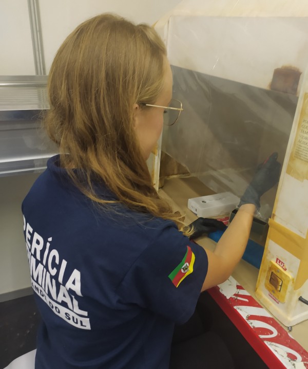 Perita com camiseta do IGP manipula pipeta dentro de capela de exaustão