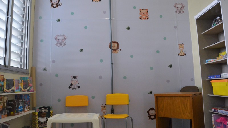 Sala com bichinhos de papel de parede, cadeiras coloridas e estante com livros e brinquedos