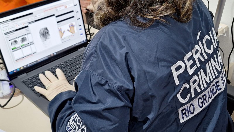 Fotografia mostra servidora com jaqueta do IGP coletando digitais de detenta