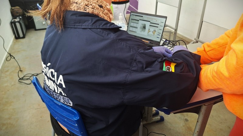 Fotografia de agente do Instituto-Geral de Perícias coletando impressões digitais durante o mutirão, para encaminhamento da Carteira de Identidade.